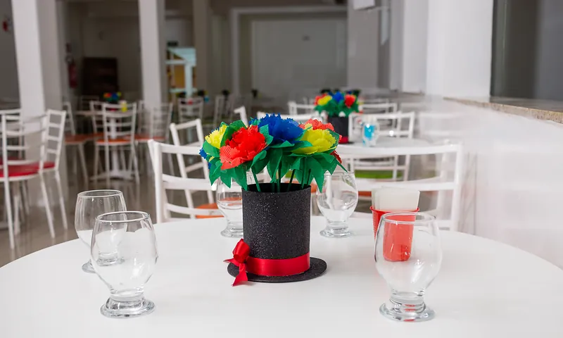 Centro de mesa com cartola e flores coloridas sobre mesa branca com taças