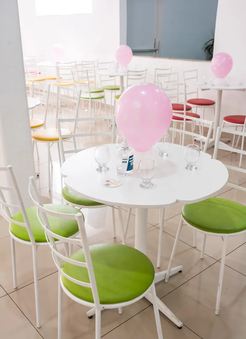 Mesa dos convidados com balão rosa, taças e cadeiras de assento verde